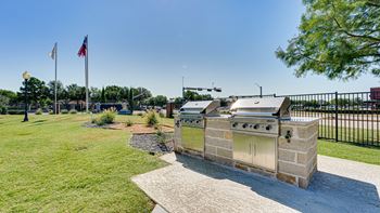 A stone structure with a grill on top is in the middle of a grassy area.